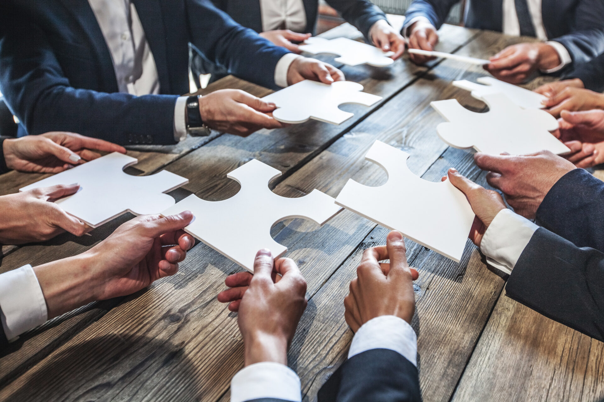 Business people and puzzle on wooden table, teamwork concept